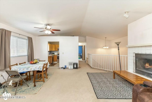 carpeted living room with a tiled fireplace, vaulted ceiling, and ceiling fan