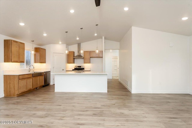 kitchen featuring a center island, light countertops, appliances with stainless steel finishes, a sink, and wall chimney range hood