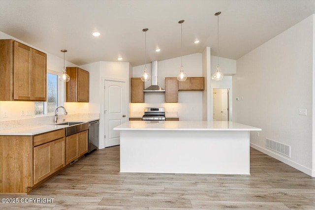 kitchen with stainless steel appliances, light countertops, a kitchen island, and wall chimney range hood