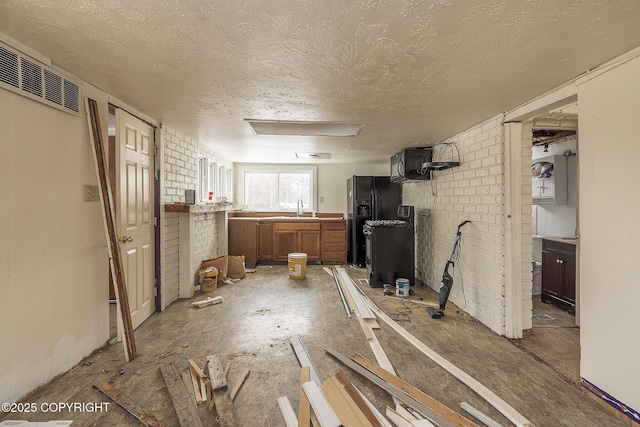 kitchen featuring visible vents, brown cabinetry, a sink, a textured ceiling, and brick wall