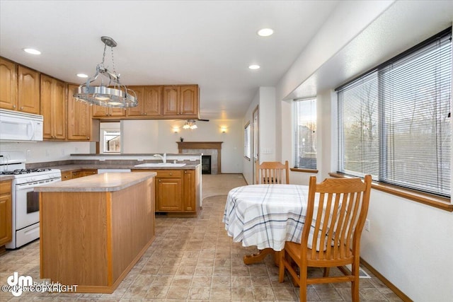 kitchen with a tile fireplace, decorative light fixtures, sink, a center island, and white appliances