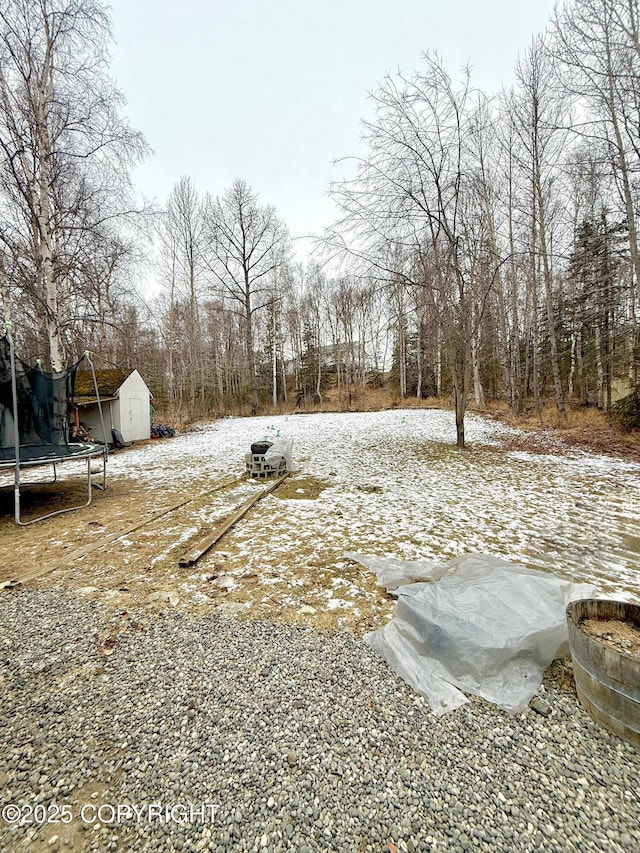 snowy yard featuring a trampoline, an outbuilding, and a storage shed