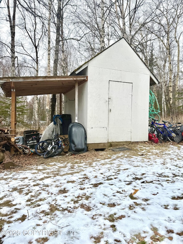 snow covered structure featuring a storage shed and an outbuilding