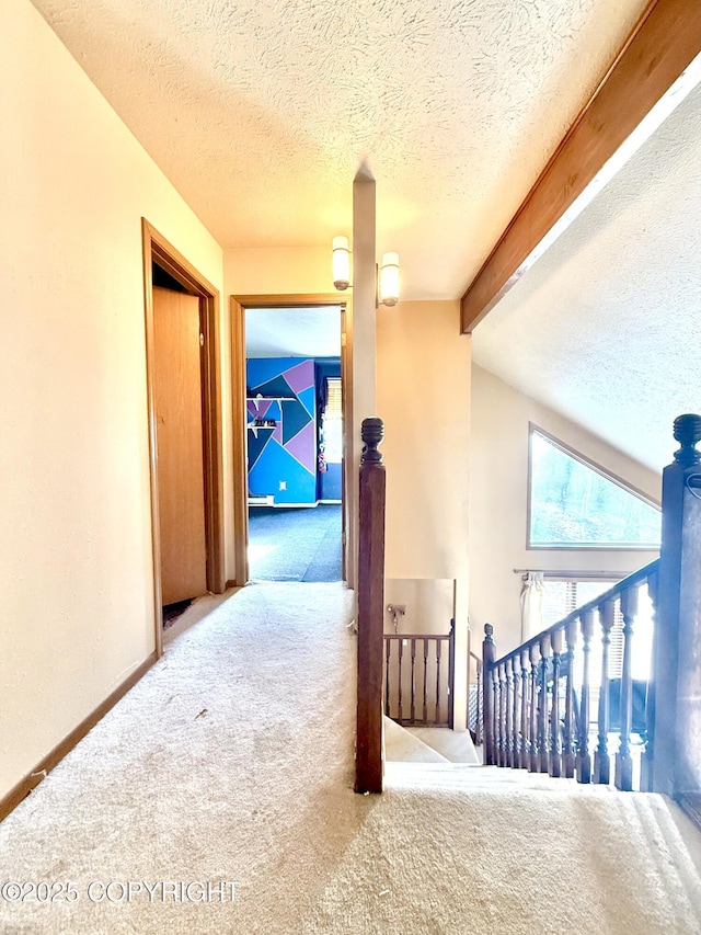 corridor featuring baseboards, vaulted ceiling with beams, a textured ceiling, an upstairs landing, and carpet floors