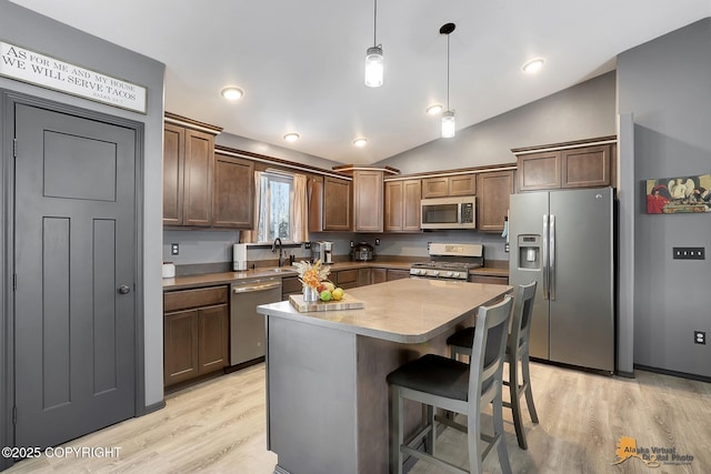 kitchen featuring vaulted ceiling, a kitchen island, appliances with stainless steel finishes, hanging light fixtures, and light hardwood / wood-style floors