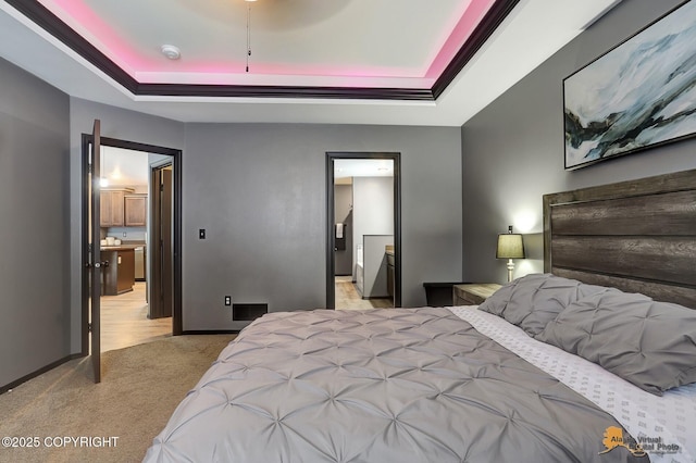 bedroom featuring light colored carpet, a raised ceiling, and ensuite bath