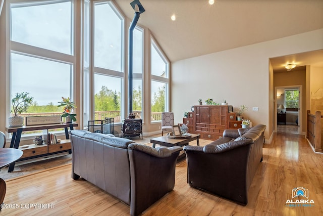 living area with a wood stove, high vaulted ceiling, and light wood finished floors