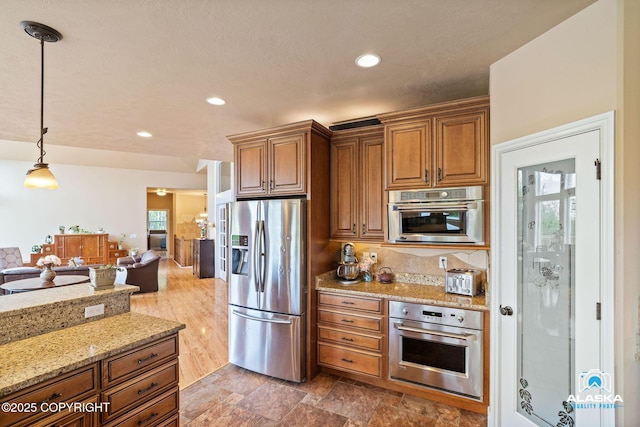 kitchen with appliances with stainless steel finishes, brown cabinetry, pendant lighting, light stone counters, and recessed lighting