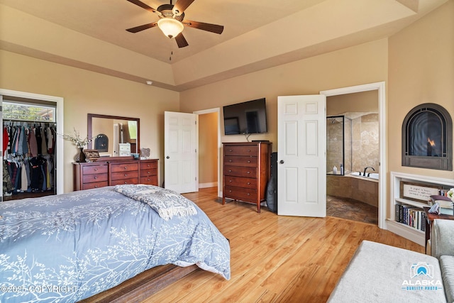 bedroom featuring wood finished floors, a walk in closet, a closet, ensuite bathroom, and a ceiling fan