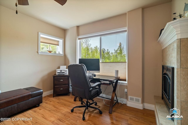 office space with a fireplace, wood finished floors, baseboards, and ceiling fan