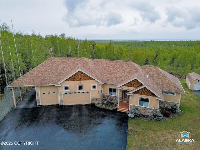 view of front of home with a forest view, driveway, stone siding, and a garage