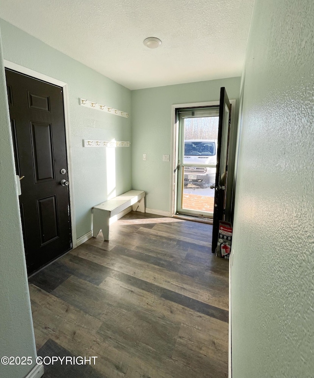 interior space featuring a textured wall, a textured ceiling, baseboards, and wood finished floors