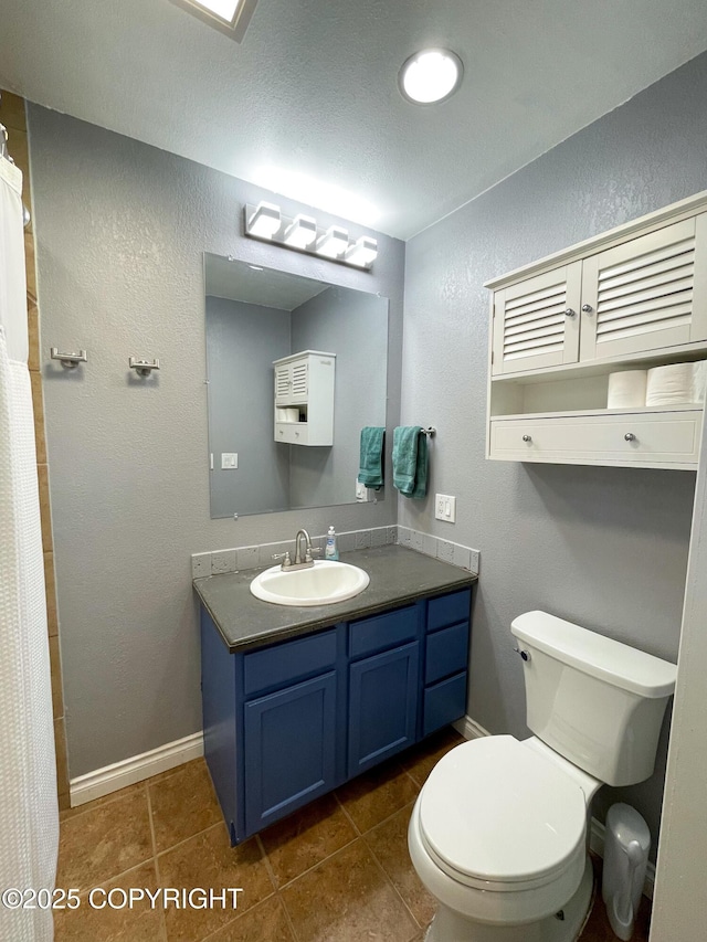 bathroom featuring baseboards, a textured wall, toilet, tile patterned flooring, and vanity