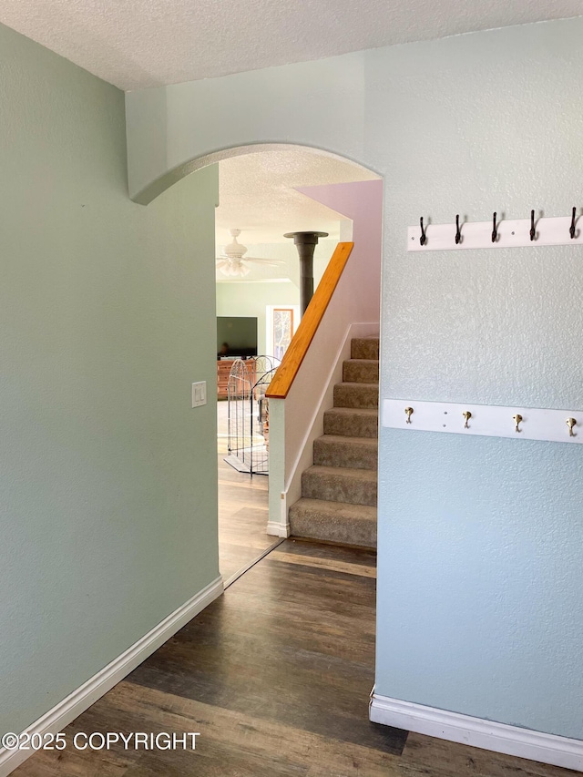 interior space with a textured ceiling, arched walkways, wood finished floors, and baseboards