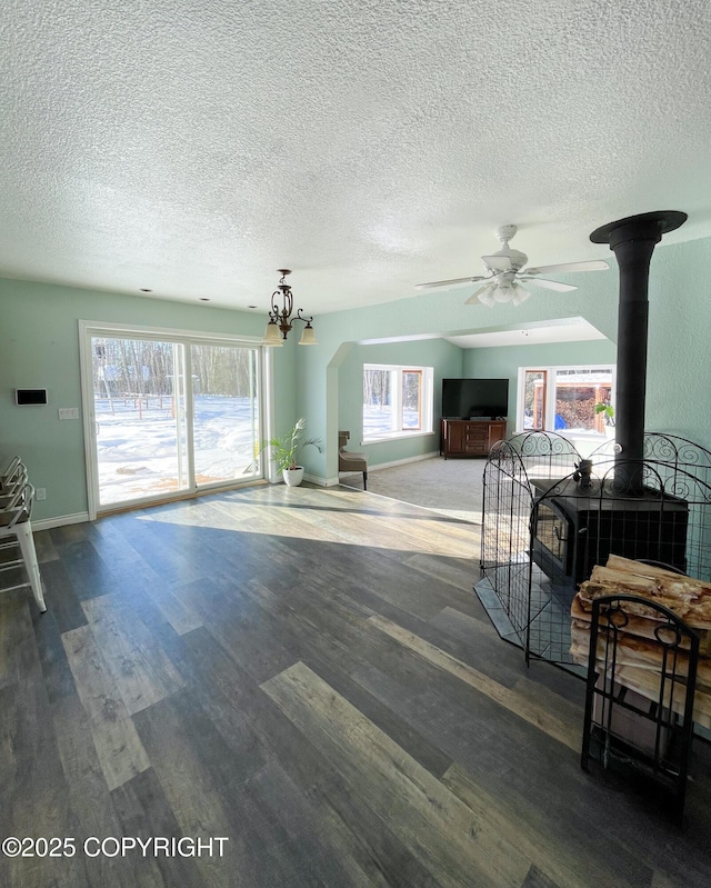 living room featuring a textured ceiling, wood finished floors, a wood stove, and baseboards