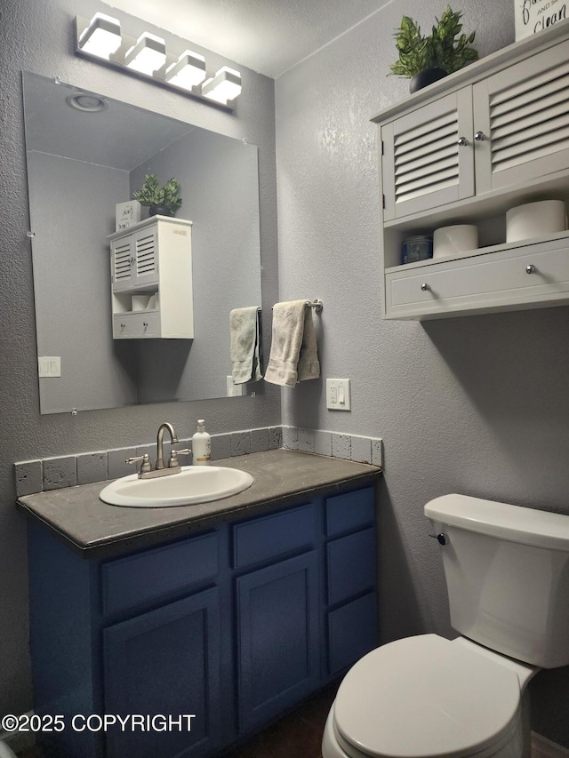 bathroom with a textured wall, vanity, and toilet