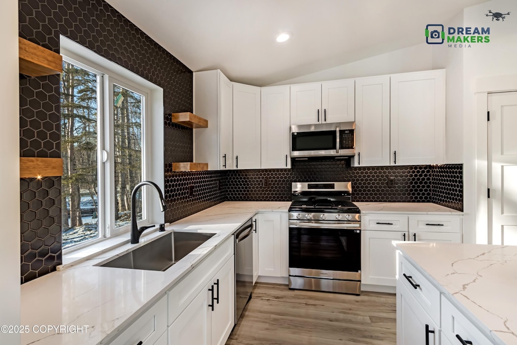 kitchen with vaulted ceiling, sink, stainless steel appliances, white cabinets, and light stone countertops