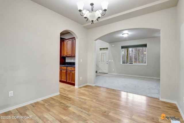 unfurnished dining area with light wood-style floors, baseboards, and an inviting chandelier