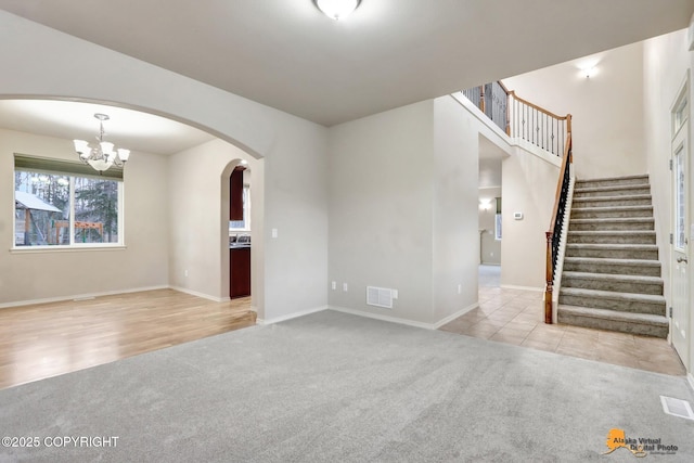 carpeted spare room featuring arched walkways, visible vents, a notable chandelier, and stairs