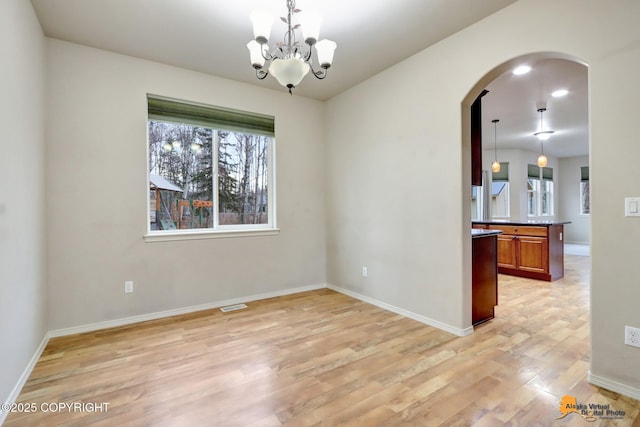 unfurnished dining area with baseboards, visible vents, arched walkways, an inviting chandelier, and light wood-type flooring