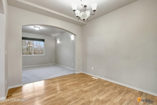 empty room featuring baseboards, arched walkways, a chandelier, and wood finished floors