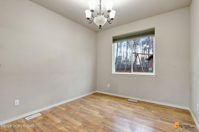 spare room featuring baseboards, light wood-style floors, visible vents, and an inviting chandelier