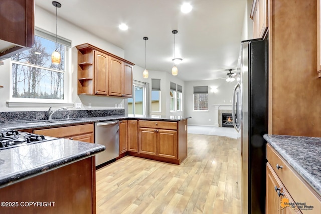 kitchen featuring stainless steel appliances, hanging light fixtures, a sink, and light wood-style flooring