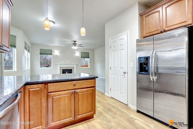 kitchen featuring stainless steel appliances, a ceiling fan, dark stone countertops, light wood-type flooring, and a lit fireplace