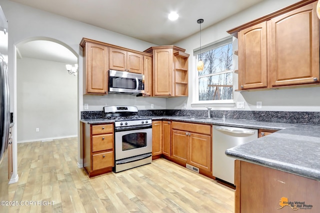 kitchen with stainless steel appliances, light wood-type flooring, hanging light fixtures, and arched walkways