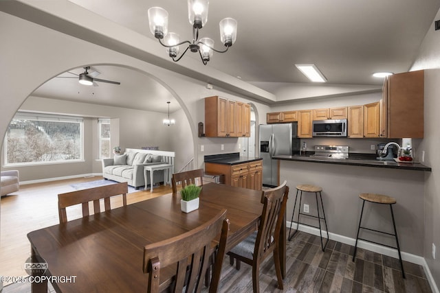 dining area featuring dark hardwood / wood-style floors, lofted ceiling, sink, and ceiling fan with notable chandelier