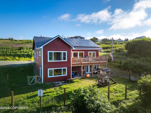 rear view of property with a lawn, a deck, french doors, metal roof, and solar panels