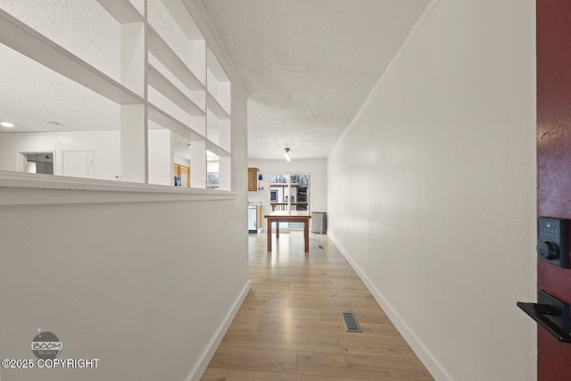 hallway featuring light hardwood / wood-style flooring, a textured ceiling, and ornamental molding