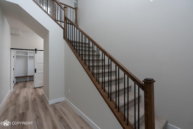 stairway featuring a barn door, wood finished floors, a high ceiling, and baseboards