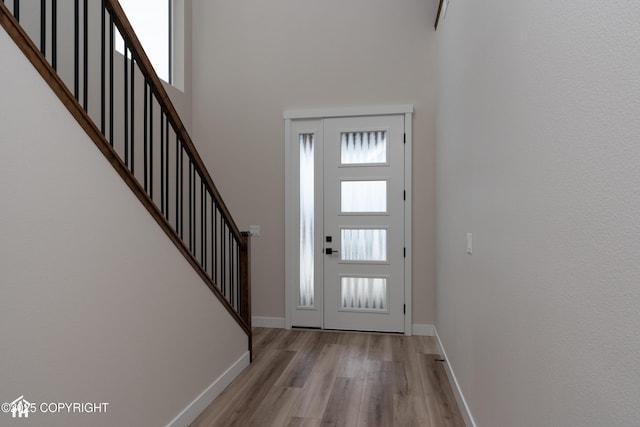 foyer featuring stairs, a towering ceiling, a wealth of natural light, and light wood-style floors