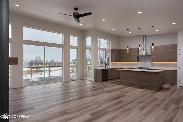 kitchen with decorative light fixtures, light countertops, a kitchen island, wall chimney range hood, and modern cabinets