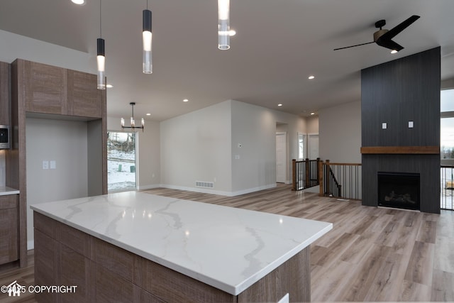 kitchen with a kitchen island, open floor plan, hanging light fixtures, light stone countertops, and modern cabinets