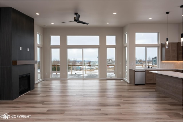 unfurnished living room featuring light wood-type flooring, a wealth of natural light, a large fireplace, and a high ceiling