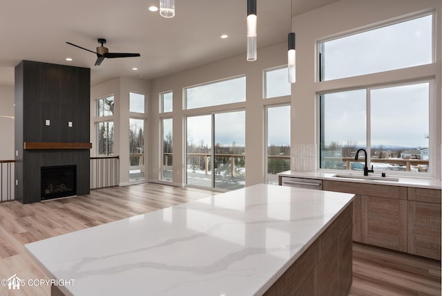 kitchen featuring open floor plan, a center island, hanging light fixtures, light stone countertops, and a sink
