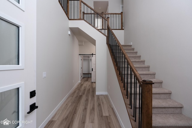 stairs featuring wood finished floors, a towering ceiling, baseboards, and a barn door