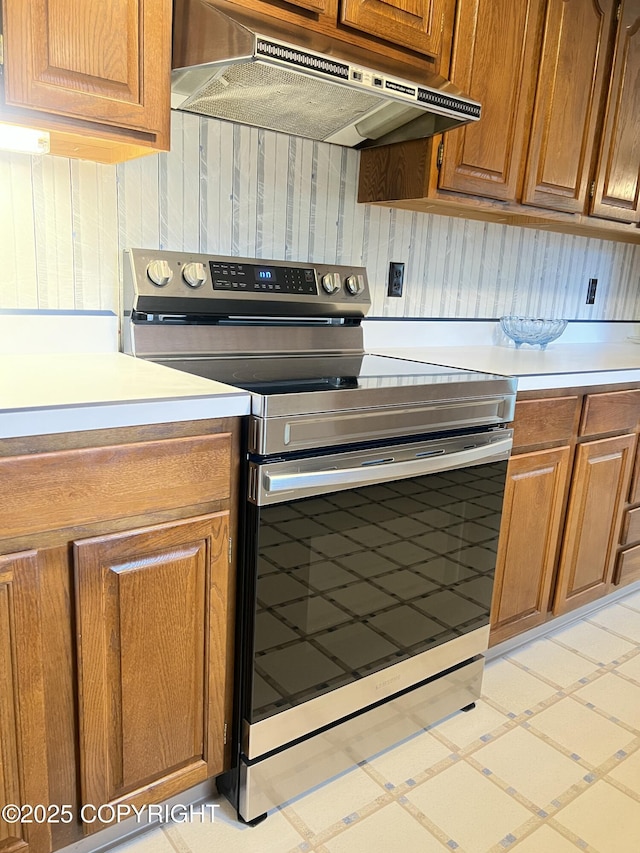 2707 W 31st Ave, Anchorage, AK 99517 - kitchen featuring stainless steel electric stove, under cabinet range hood, light countertops, and brown cabinets