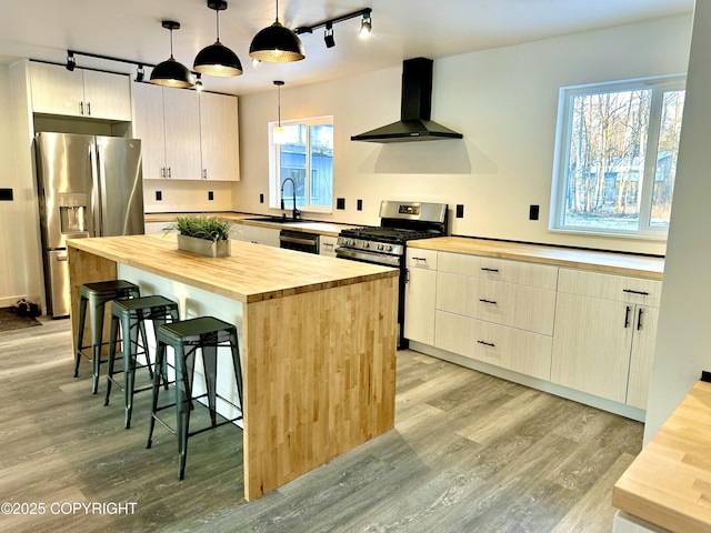 kitchen with wall chimney exhaust hood, a breakfast bar, stainless steel appliances, wooden counters, and a sink