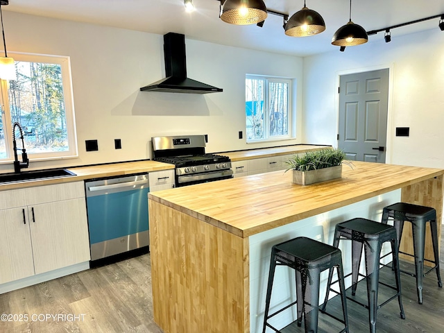 kitchen featuring dishwashing machine, stainless steel gas range oven, butcher block countertops, a sink, and wall chimney exhaust hood