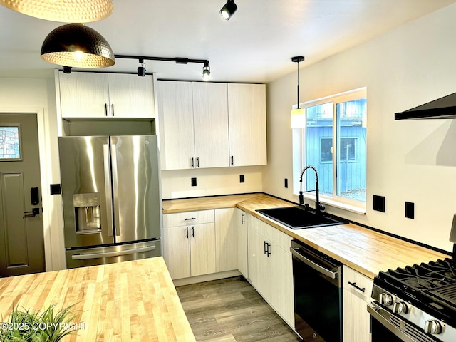 kitchen featuring appliances with stainless steel finishes, decorative light fixtures, light wood-type flooring, wooden counters, and a sink