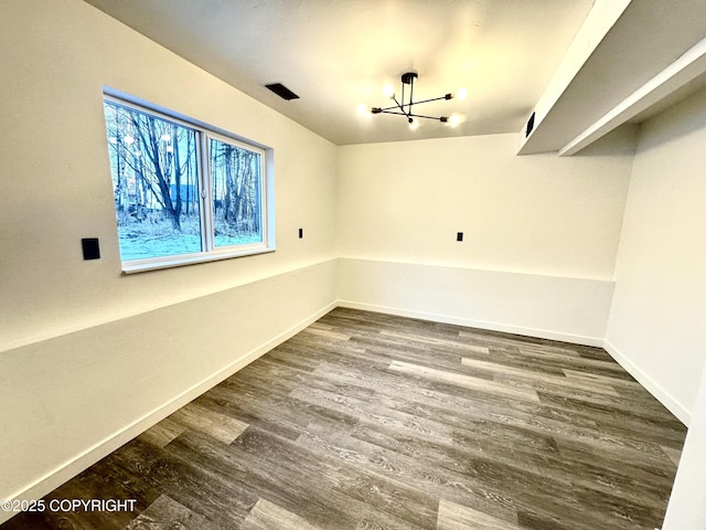 unfurnished room with an inviting chandelier, wood finished floors, visible vents, and baseboards