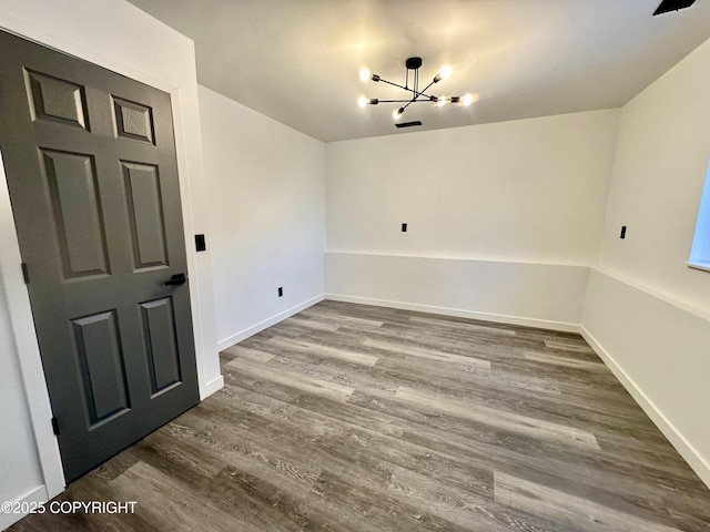 empty room featuring baseboards, dark wood-type flooring, and a notable chandelier