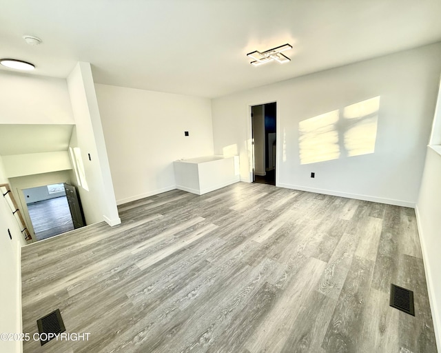 unfurnished living room with wood finished floors, visible vents, and baseboards