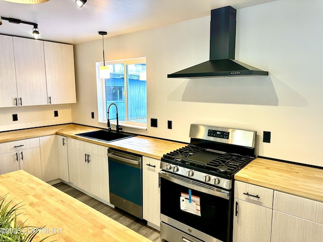 kitchen with dishwasher, butcher block counters, wall chimney range hood, a sink, and gas stove