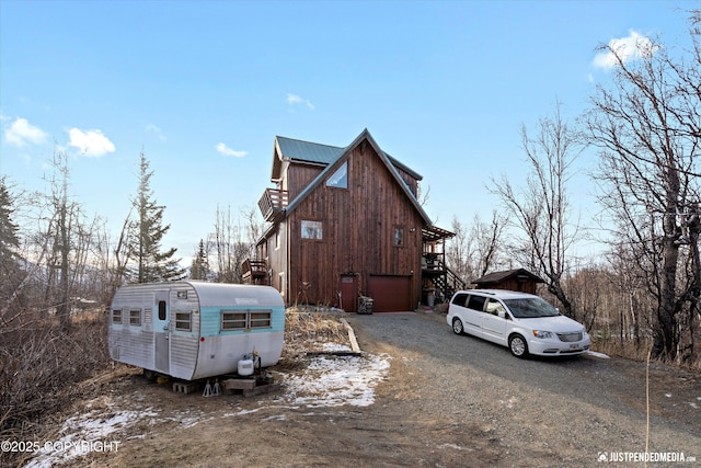 view of snowy exterior featuring dirt driveway, stairs, and a garage