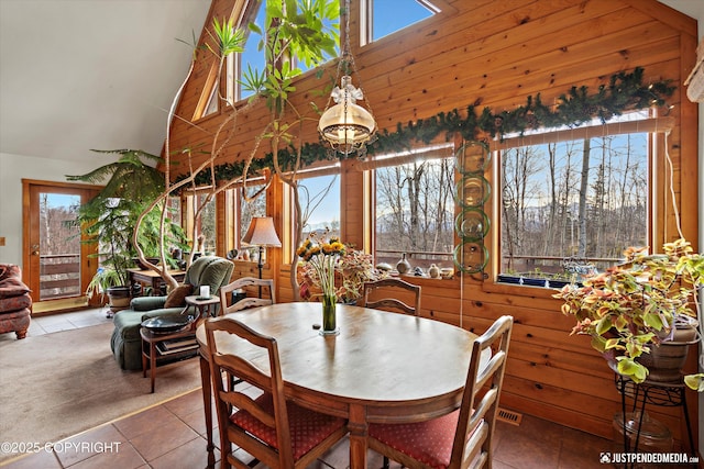 carpeted dining area featuring high vaulted ceiling, wood walls, tile patterned flooring, and visible vents