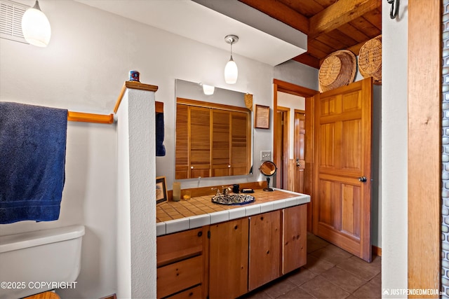 bathroom featuring toilet, a sink, tile patterned flooring, beam ceiling, and a closet